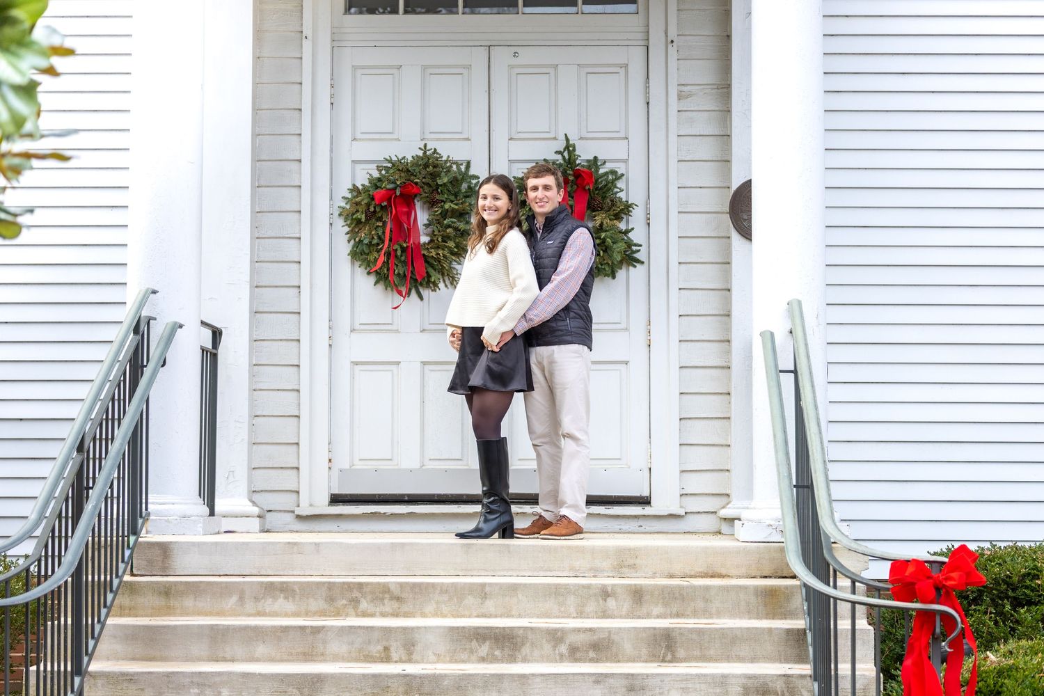 White house porch decorated for Christmas with red bows and greenery along the railing.