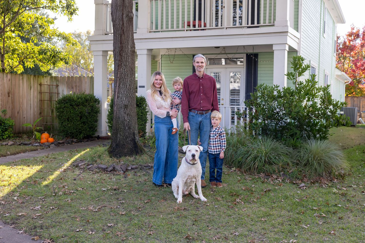 Family and dog standing in front yard of white house during fall season.