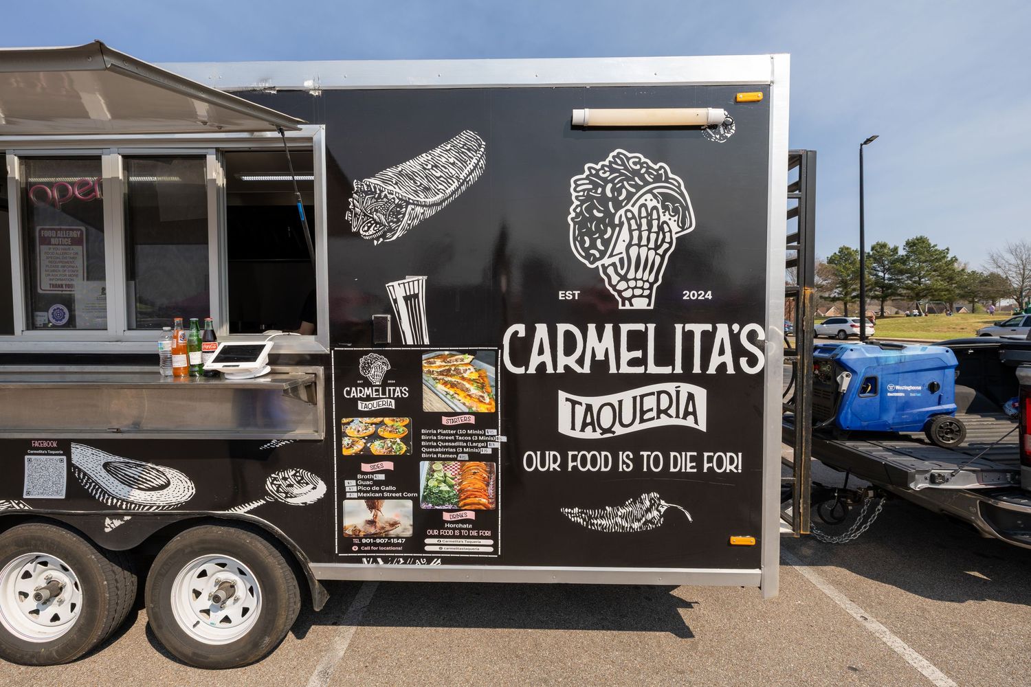 A black food truck with Carmelitas Taqueria logo and menu painted on the side parked in a parking lot.