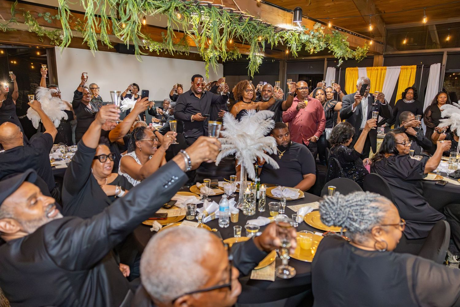 Large group dining event with guests seated at long tables in a restaurant setting.