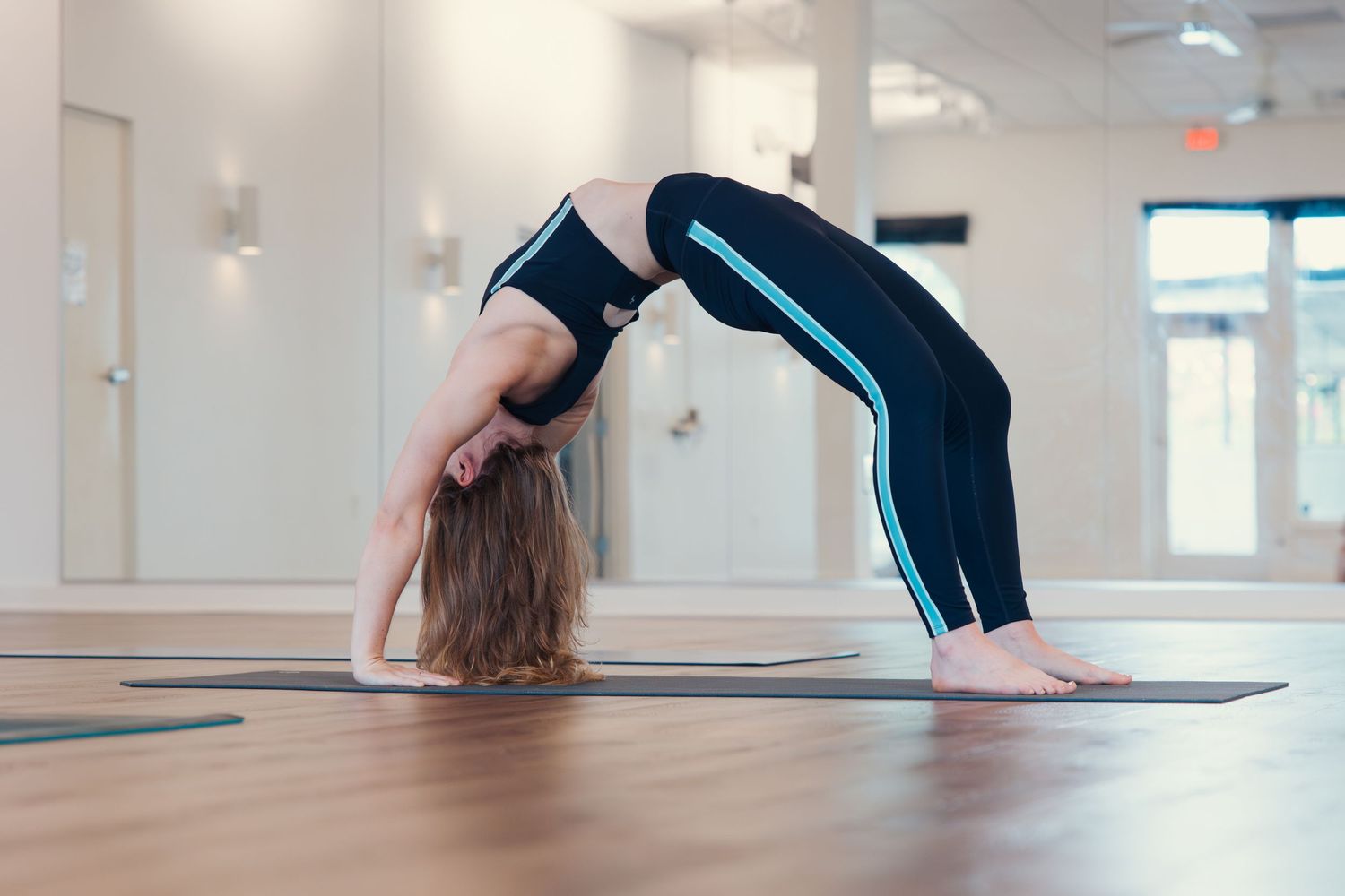 Person demonstrating wheel pose backbend on yoga mat in studio.