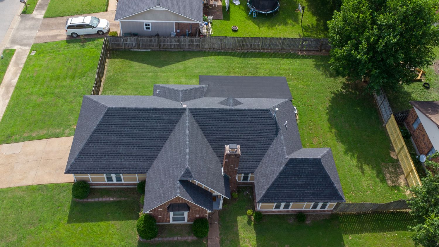 Aerial view of suburban houses with green lawns and driveways surrounded by trees on a sunny day.