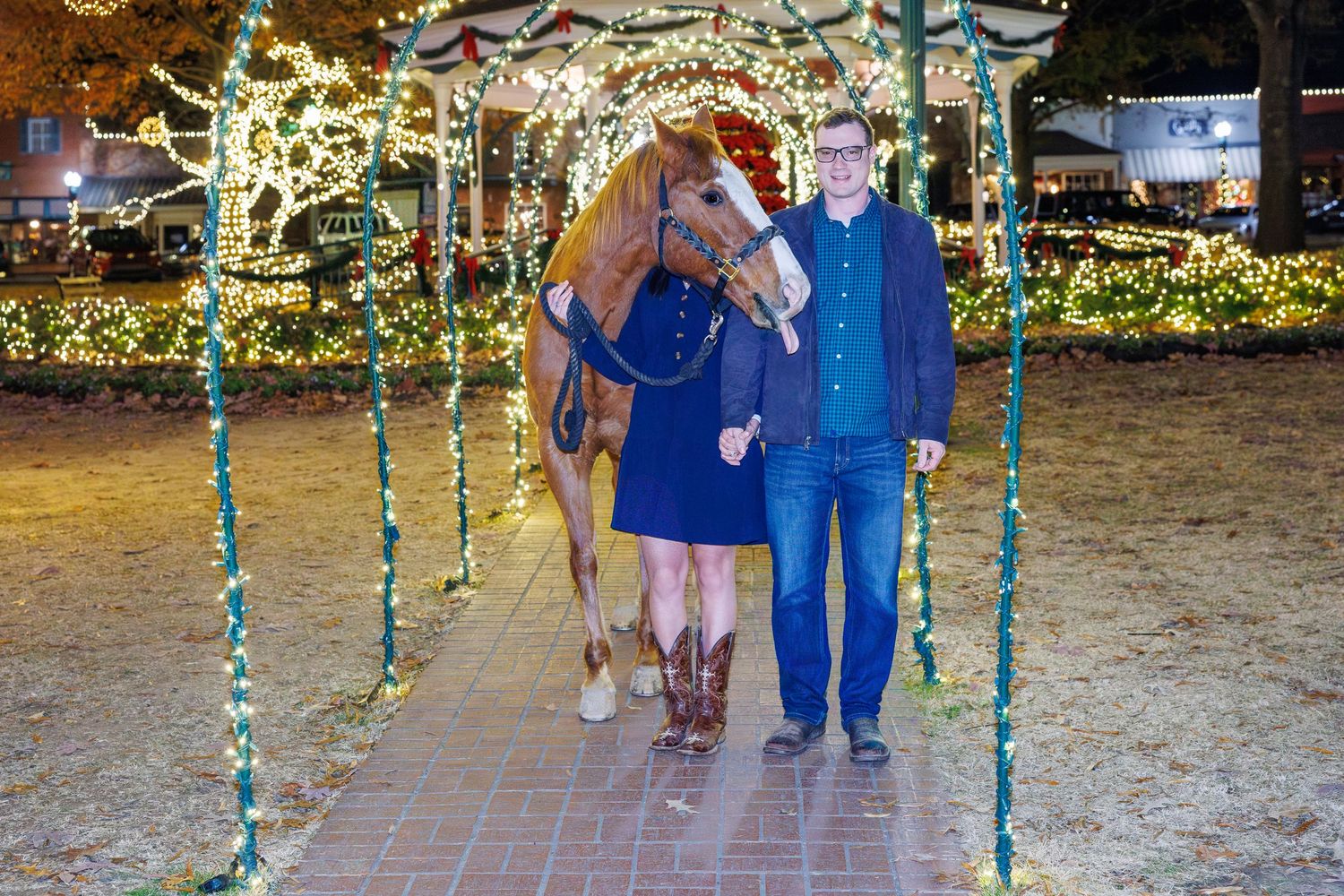 People walk through a pathway decorated with hanging teal lights and festive holiday decor.