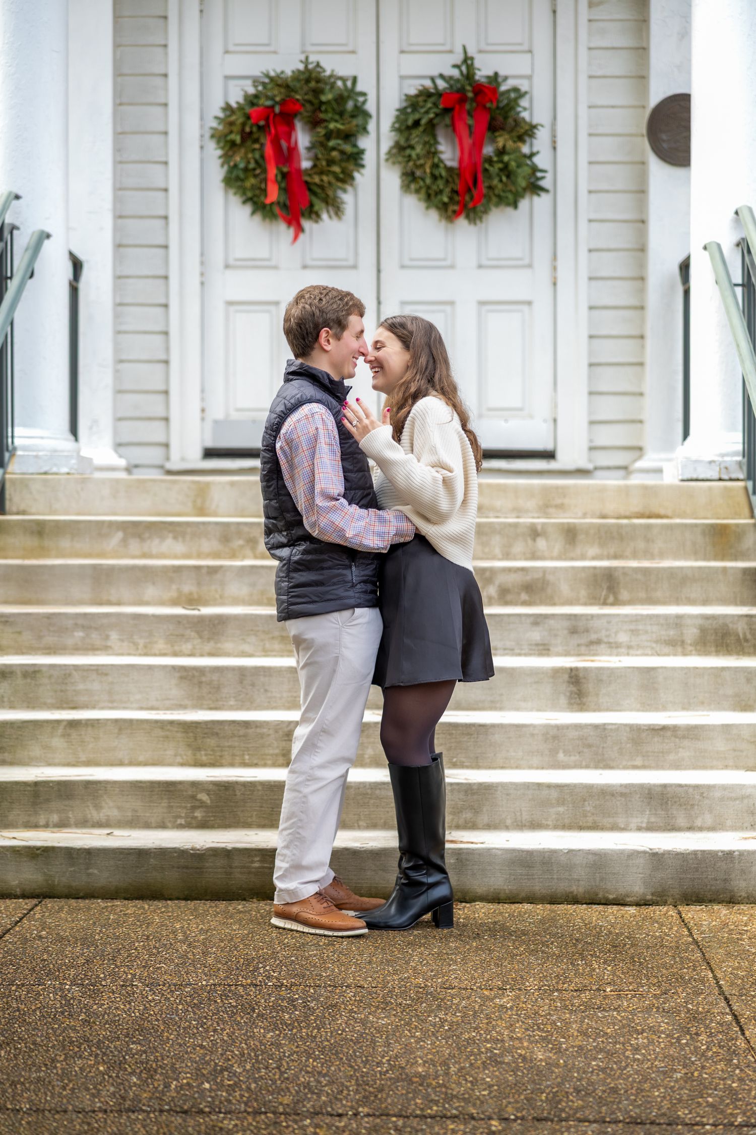 A romantic holiday proposal moment on white church steps decorated with Christmas wreaths.