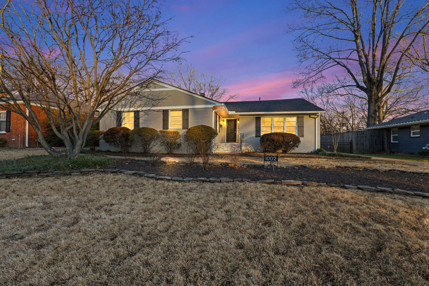 Exterior view of a modern single-story home with brown siding and white trim at sunset against bare winter trees.