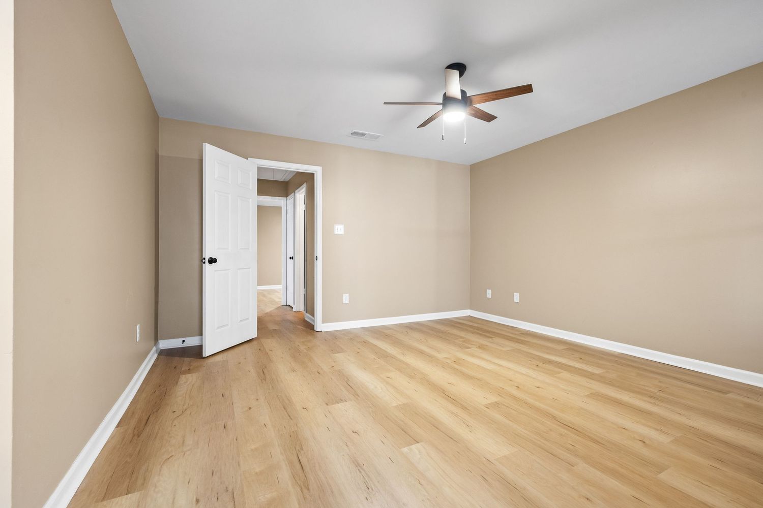Spacious room with hardwood floors and neutral walls features ceiling fan and natural lighting.