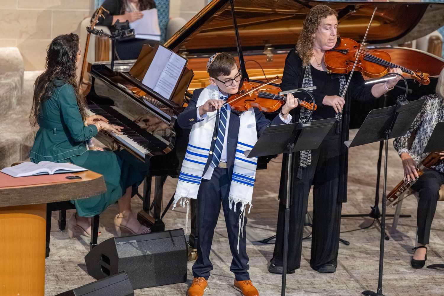 Boy in tallit plays violin at bar mitzvah ceremony with pianist and violinist accompanists.