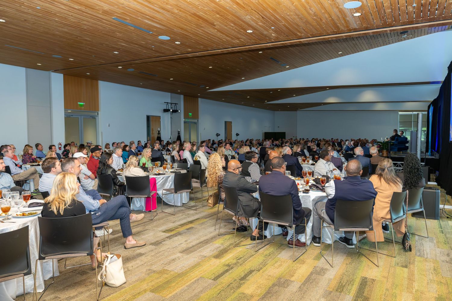 Large corporate event banquet hall filled with attendees seated at round tables during a professional conference or gala dinner.
