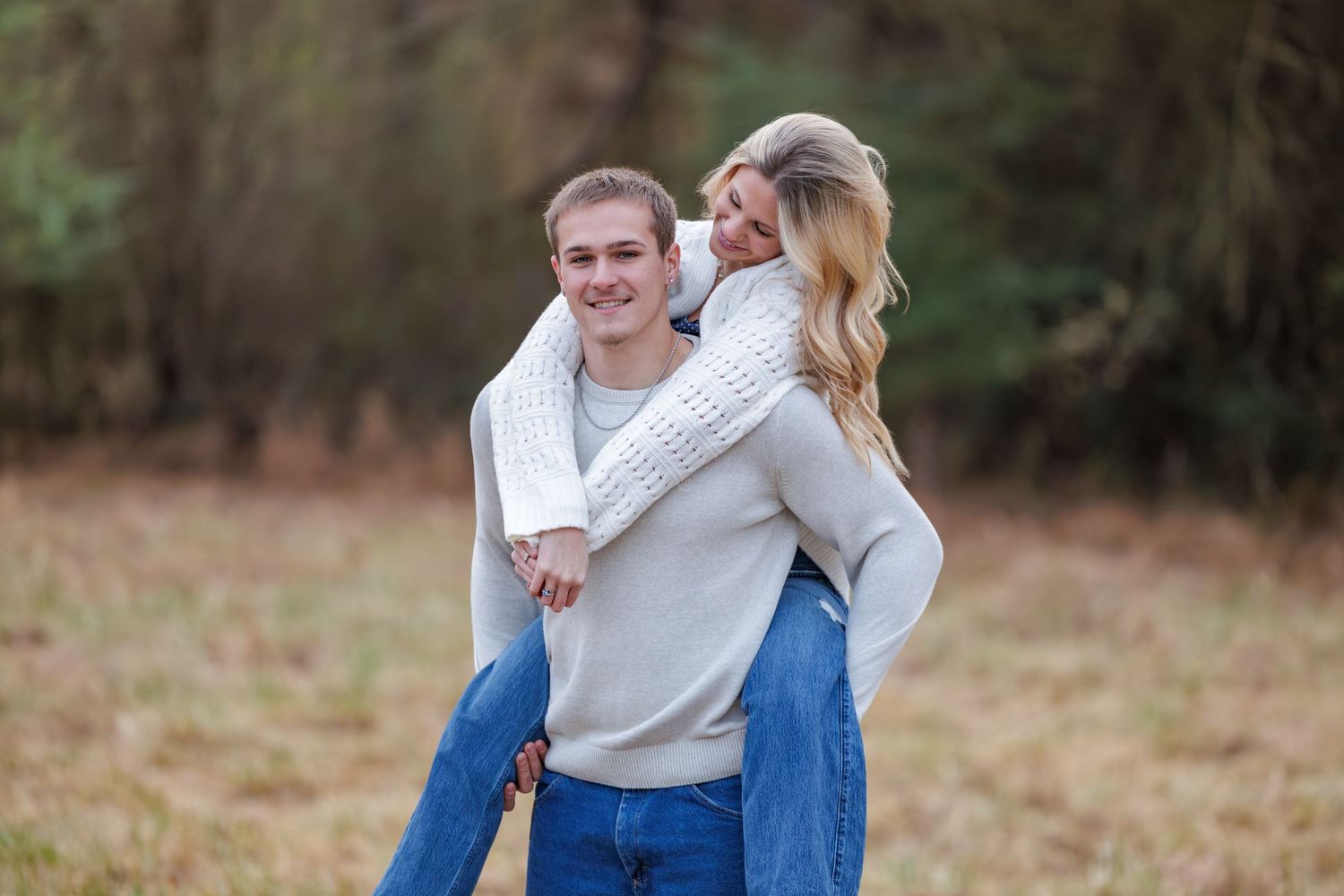 A couple in matching light sweaters and blue jeans embrace in an autumn field during a romantic photoshoot.