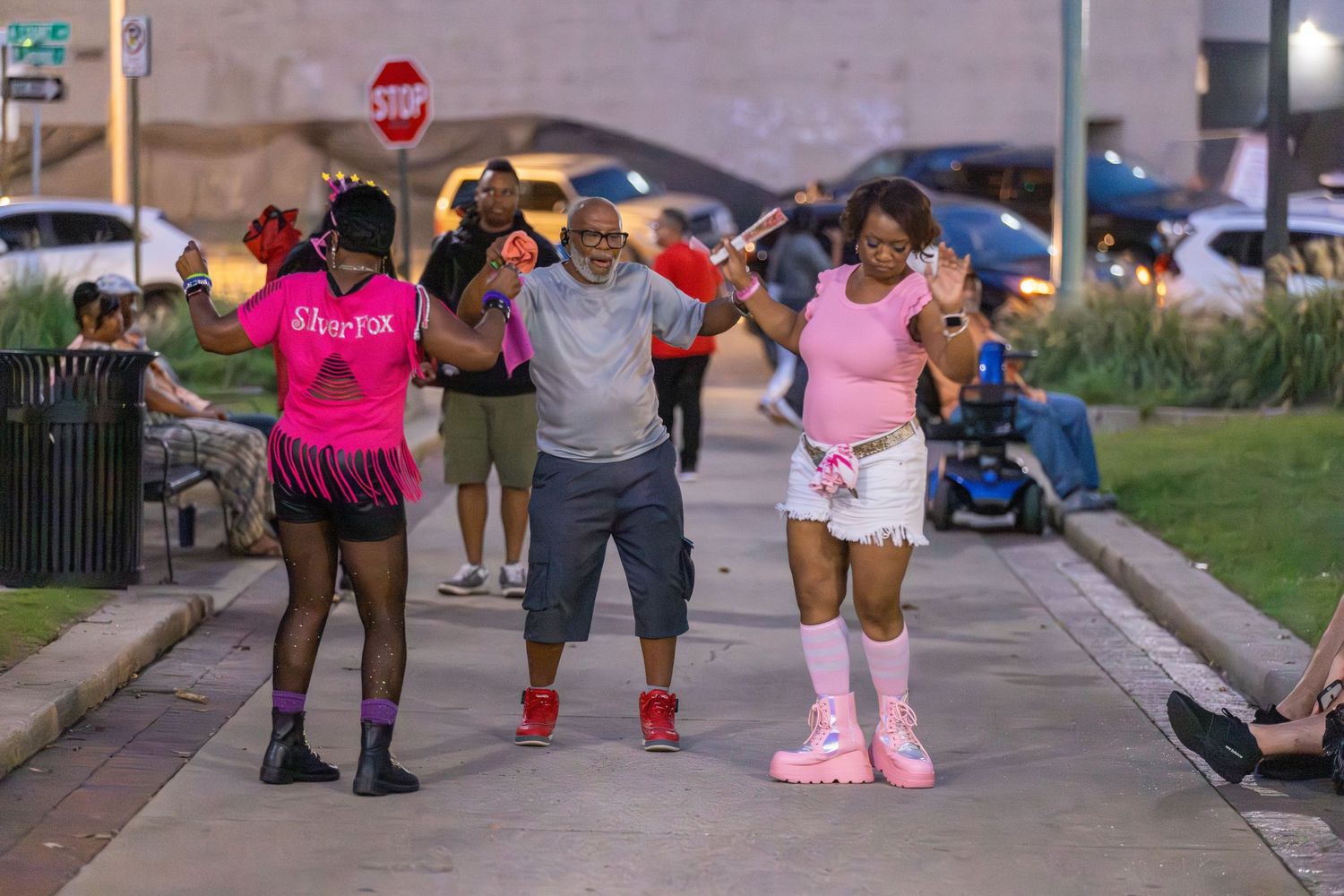 People walking and dancing together on a sidewalk during a festive outdoor event.