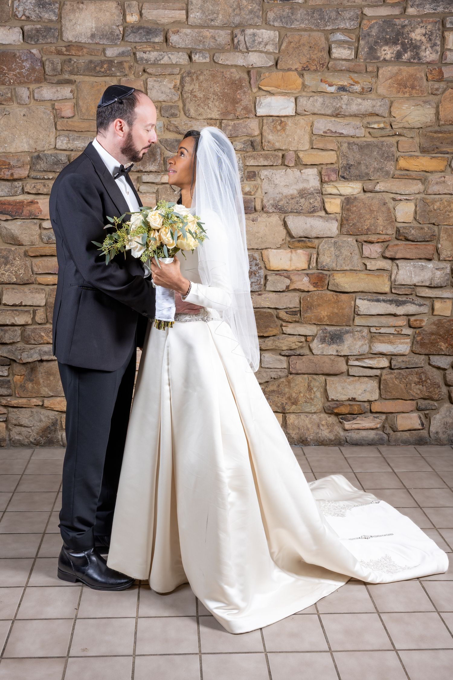 Elegant bridal portraits against textured stone wall backdrop with cream-colored wedding gown.