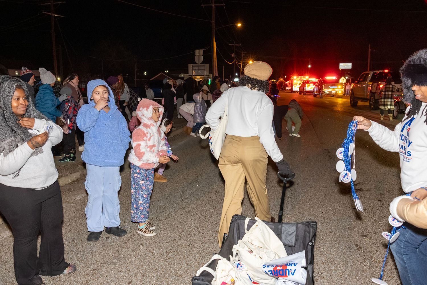 People gathered outdoors at night for a community event with emergency lights visible.