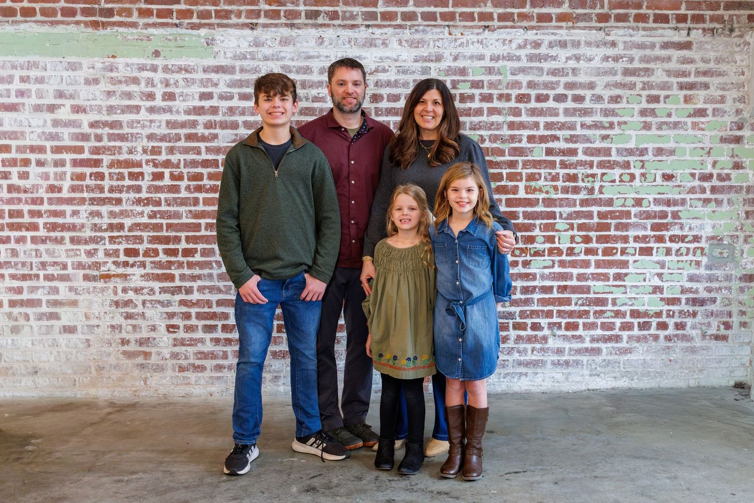 Family group poses against rustic brick wall background.