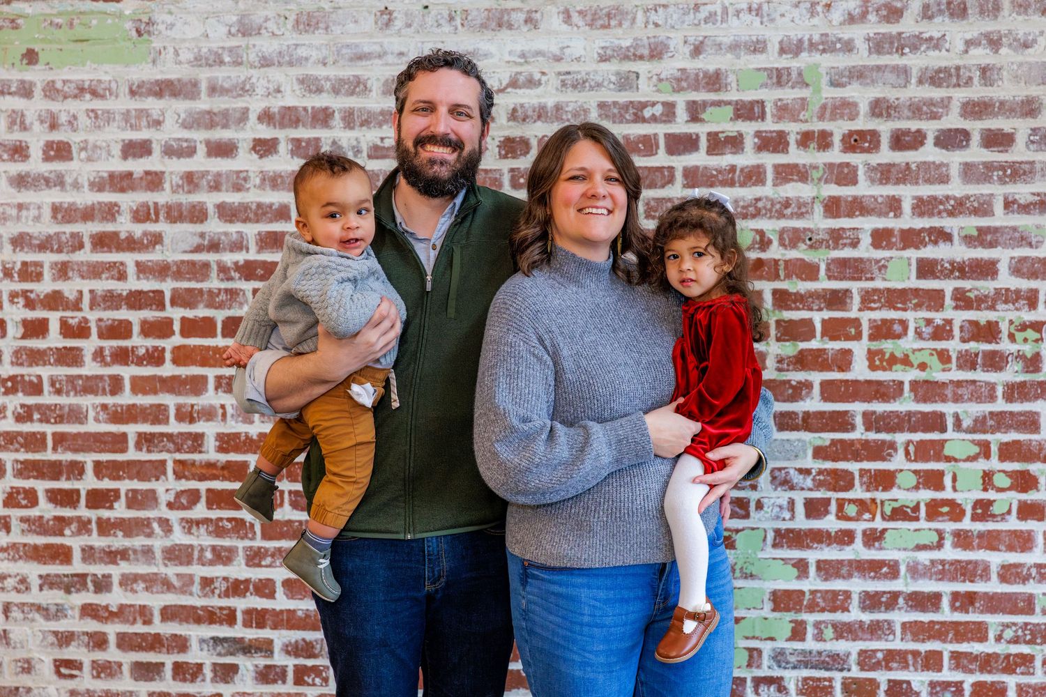Family group gathered for a photo against a weathered brick wall background.