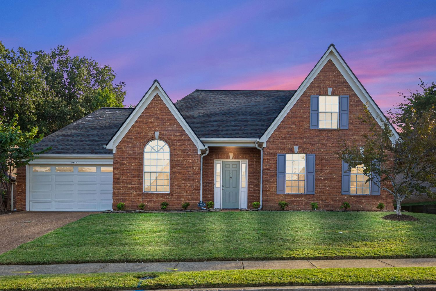Panoramic view of a brick ranch-style house with multiple windows at dusk.