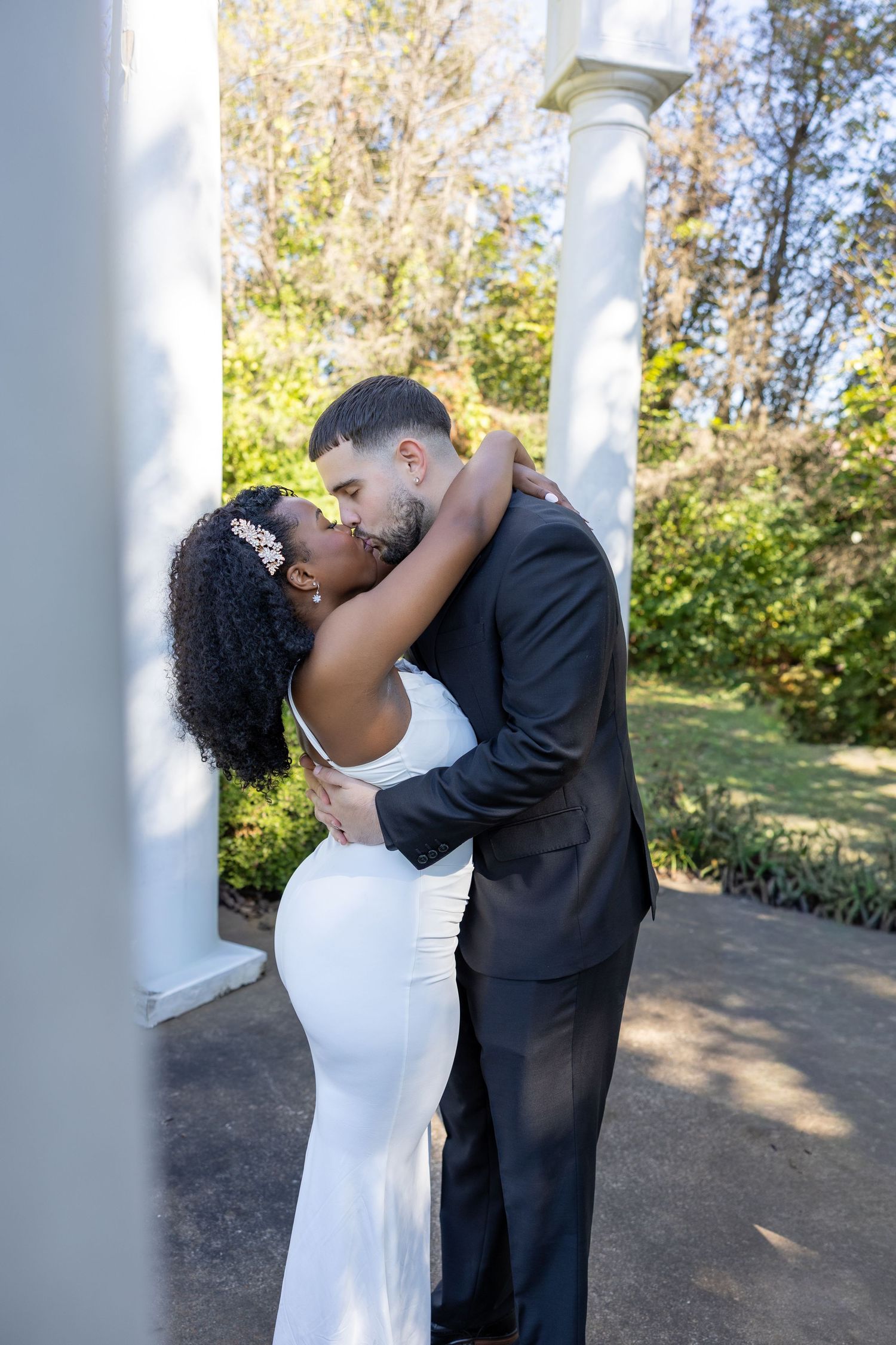 Romantic wedding couple sharing intimate moments by white pillars in an outdoor garden setting.