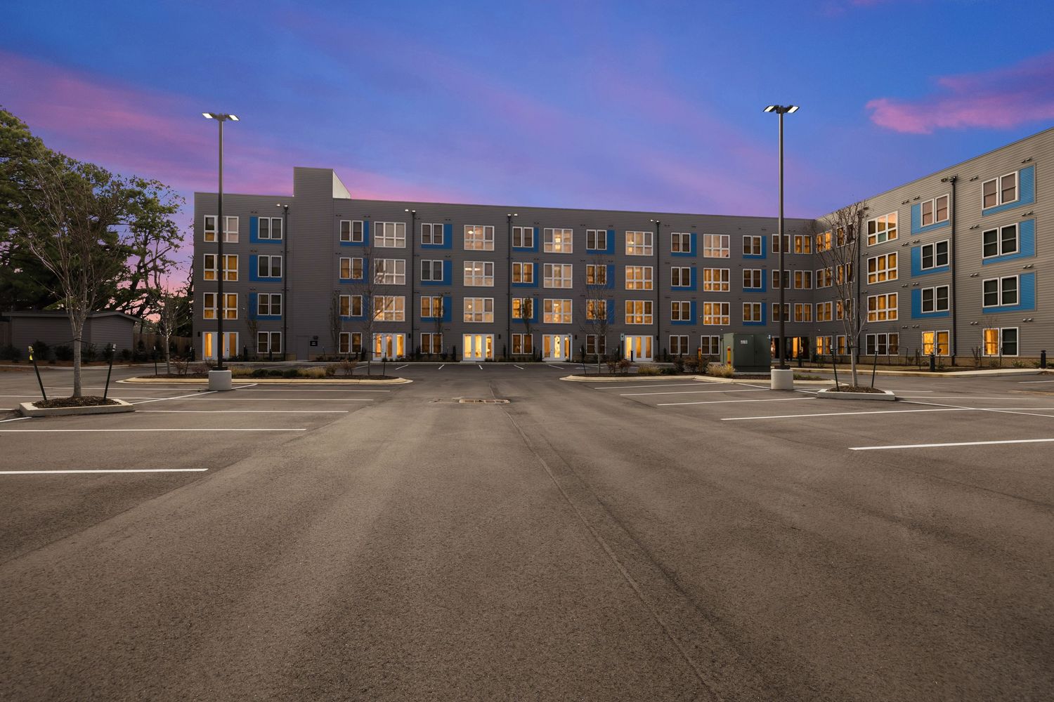 Multi-story apartment building exterior with ample parking space at sunset.