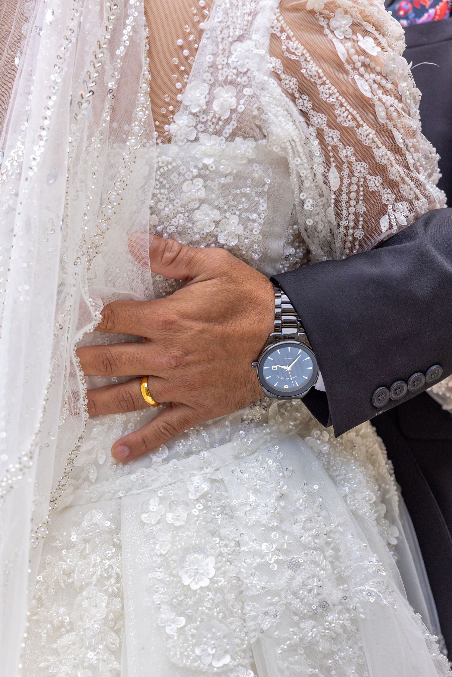 Close-up details of wedding attire showing beaded dress, watch, and gold wedding band.