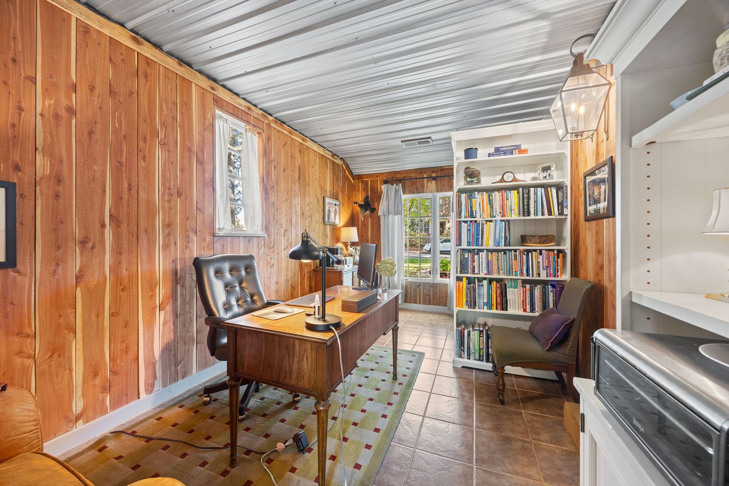 Cozy attic library room with wood paneled walls, built-in bookshelves, and sloped ceiling with skylights.