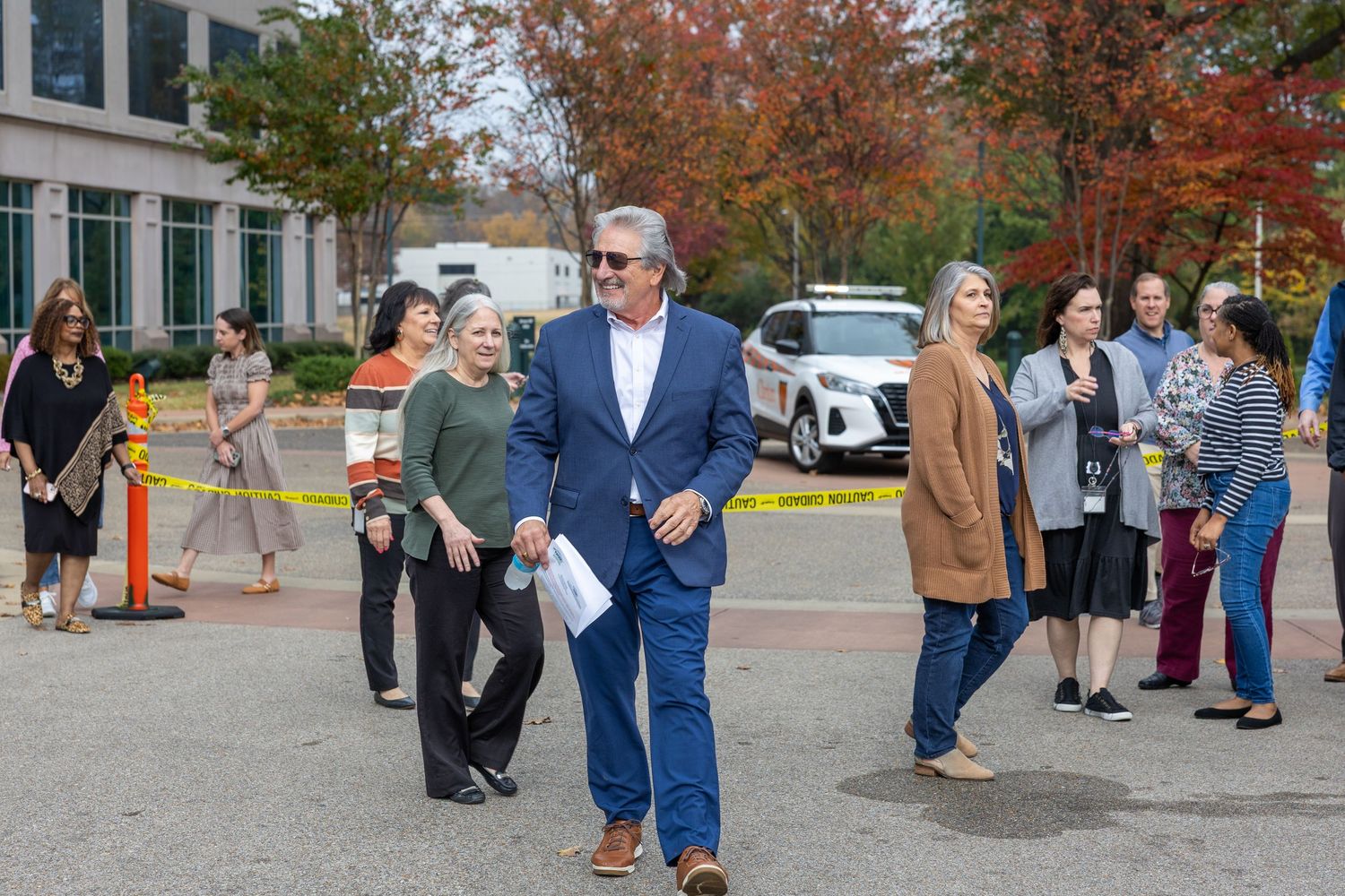 Group of attendees mingle outdoors during fall event with autumn foliage visible.