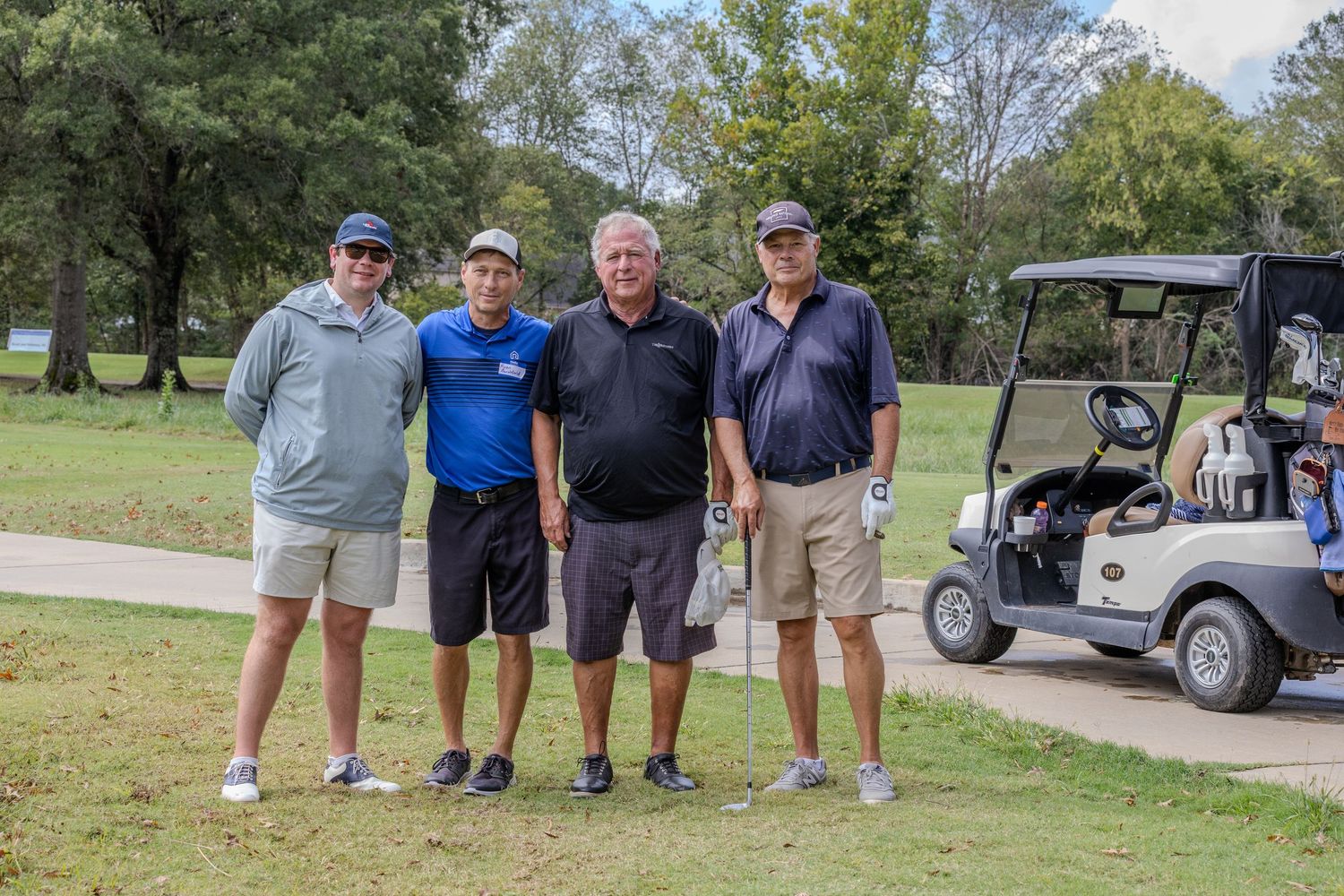 Group of golfers standing near golf carts on a sunny course.