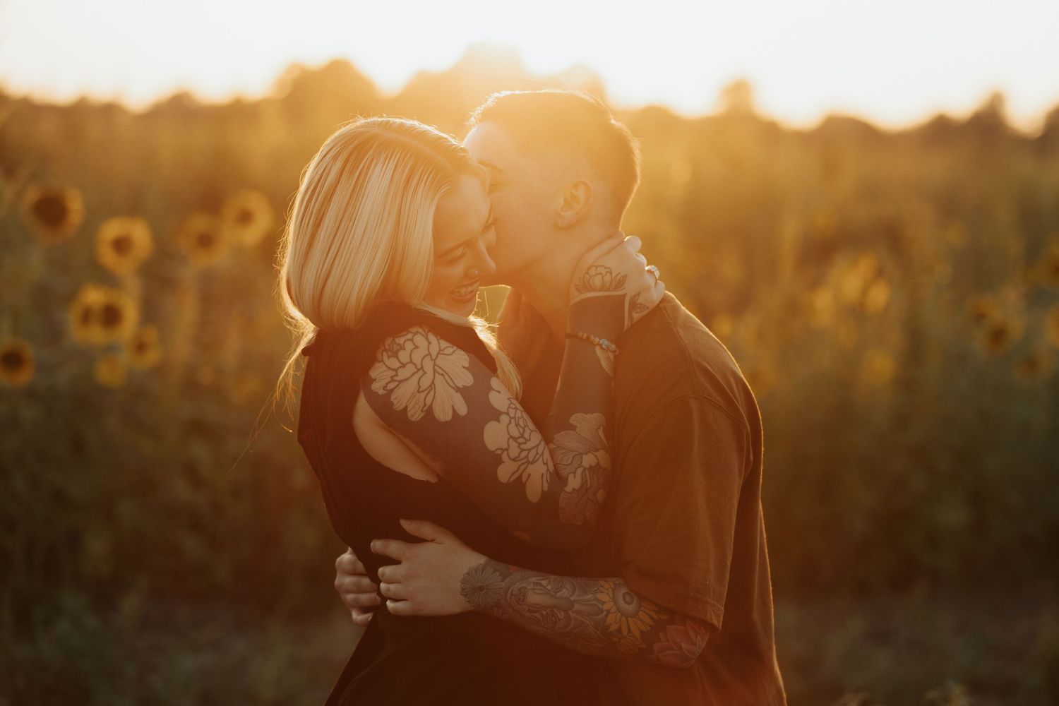 Warm sunset light illuminates a tender embrace in a field of sunflowers.