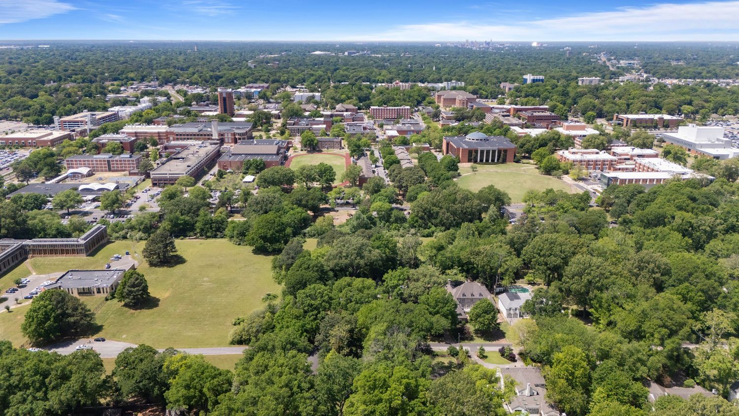 Aerial view of a lush university campus with historic brick buildings surrounded by mature trees.
