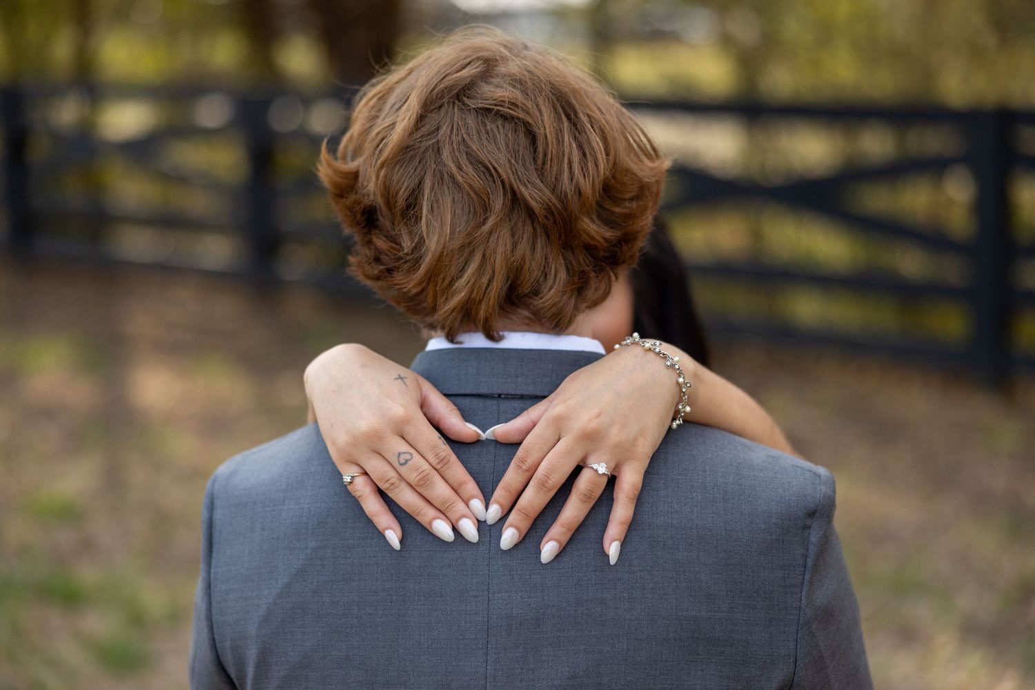 A couple embraces during a romantic outdoor photo session with a rustic wooden fence in the background.