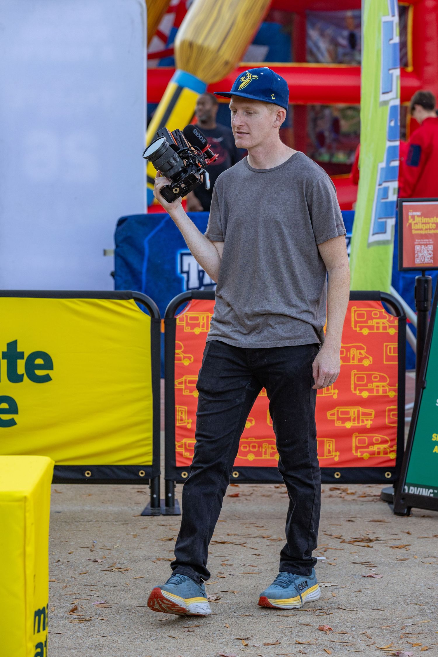 Close-up view of someone's legs wearing blue sneakers and dark pants standing near yellow carnival barriers.