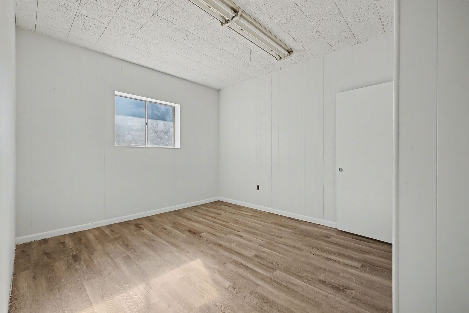 Modern white interior with exposed ceiling beams, wooden flooring, and natural light streaming through windows.