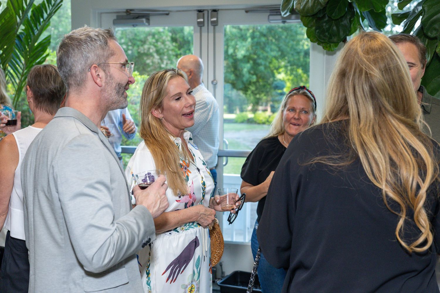 People networking and conversing at an indoor social gathering in a bright modern space with tropical plant decor.