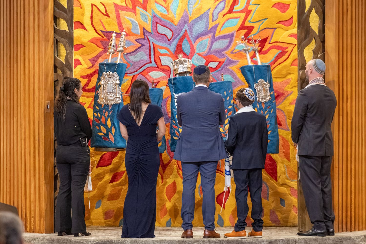 Group of people viewing a vibrant colorful mural with bold abstract design in warm yellow, orange, and blue tones.