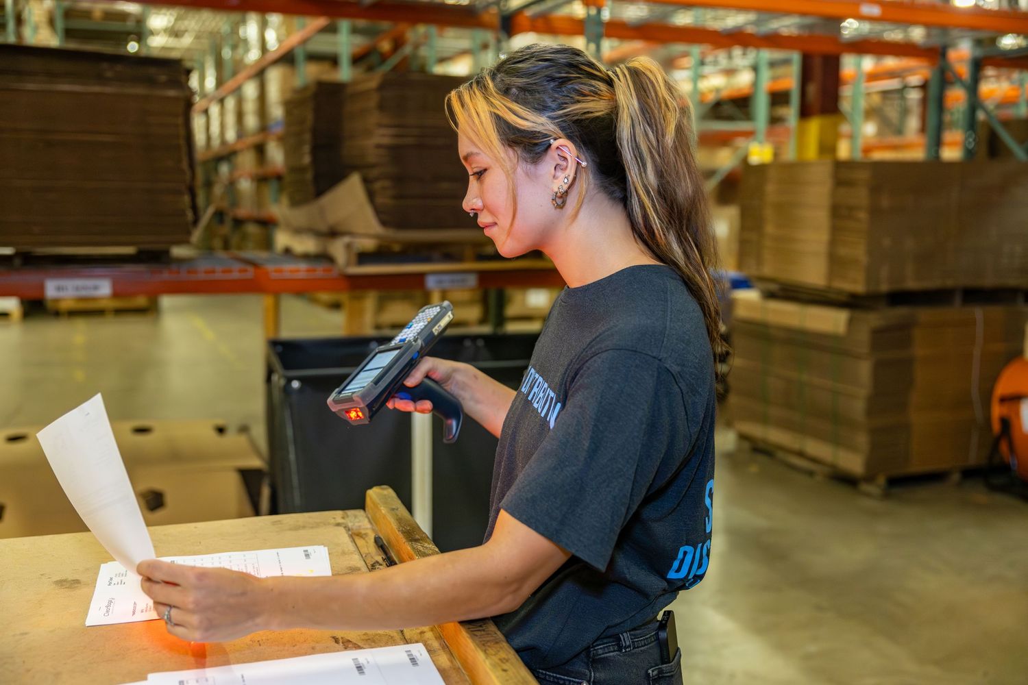 Warehouse worker reviewing paperwork while holding scanner in distribution center.
