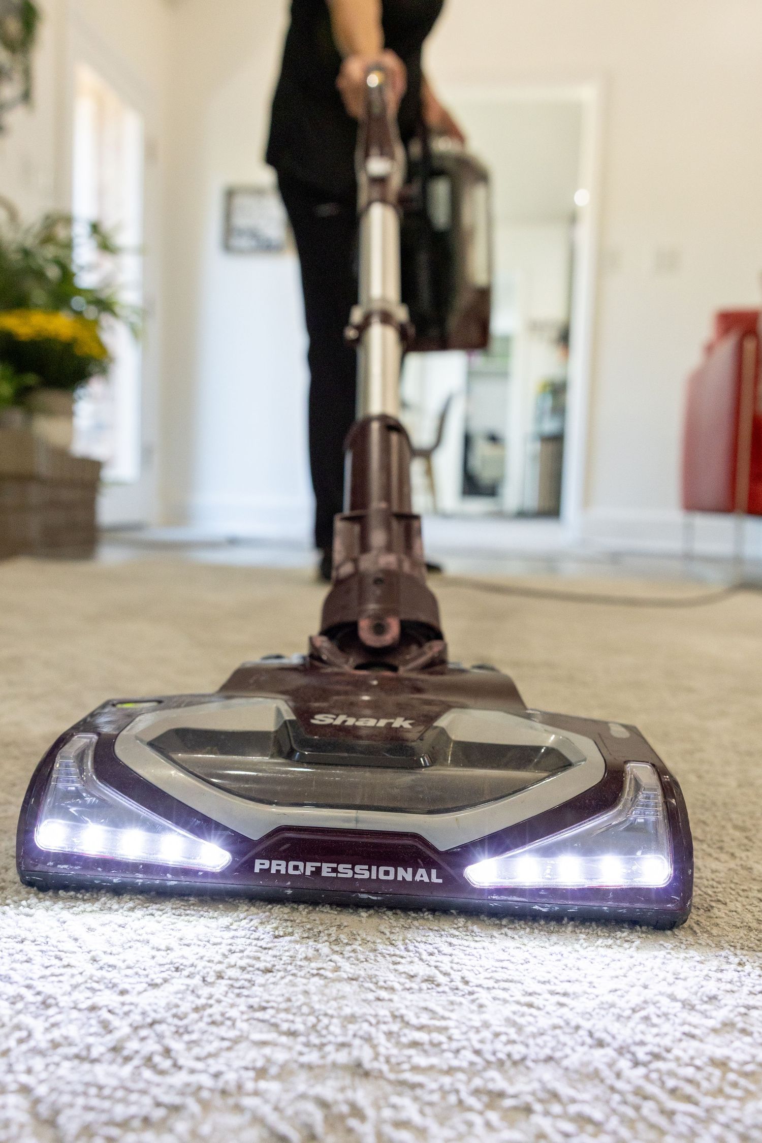 Close-up of vacuum cleaner head with LED lights on carpet during cleaning.