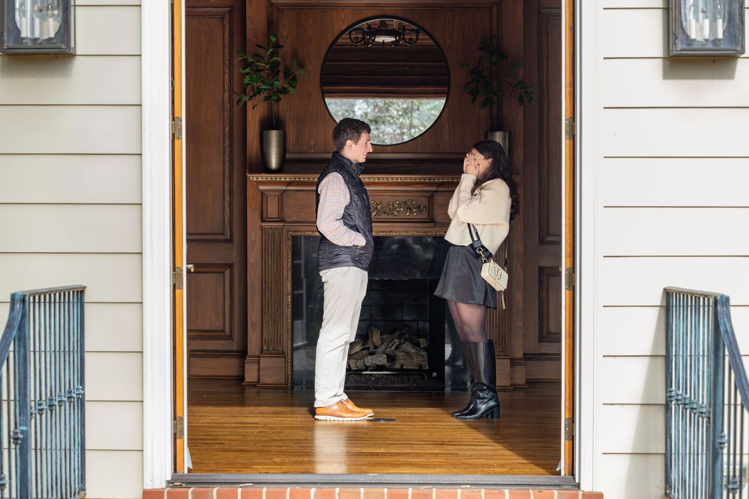 Two people stand in conversation at an elegant doorway with a round window and wooden door frame.