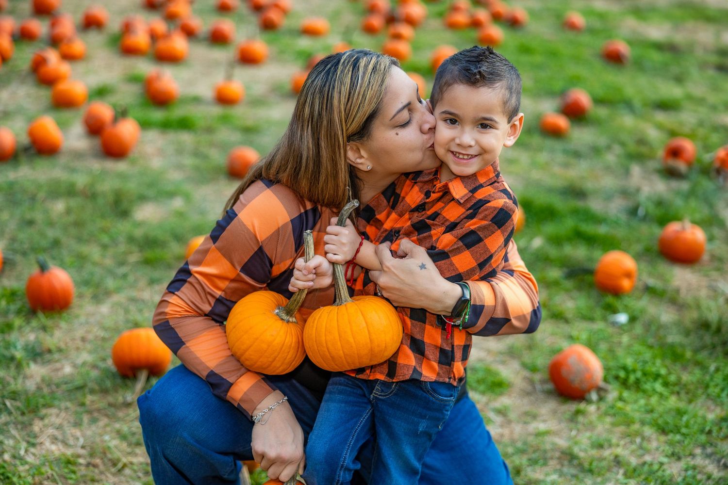 Playful autumn moments captured in pumpkin patch with orange and plaid themed outfits.