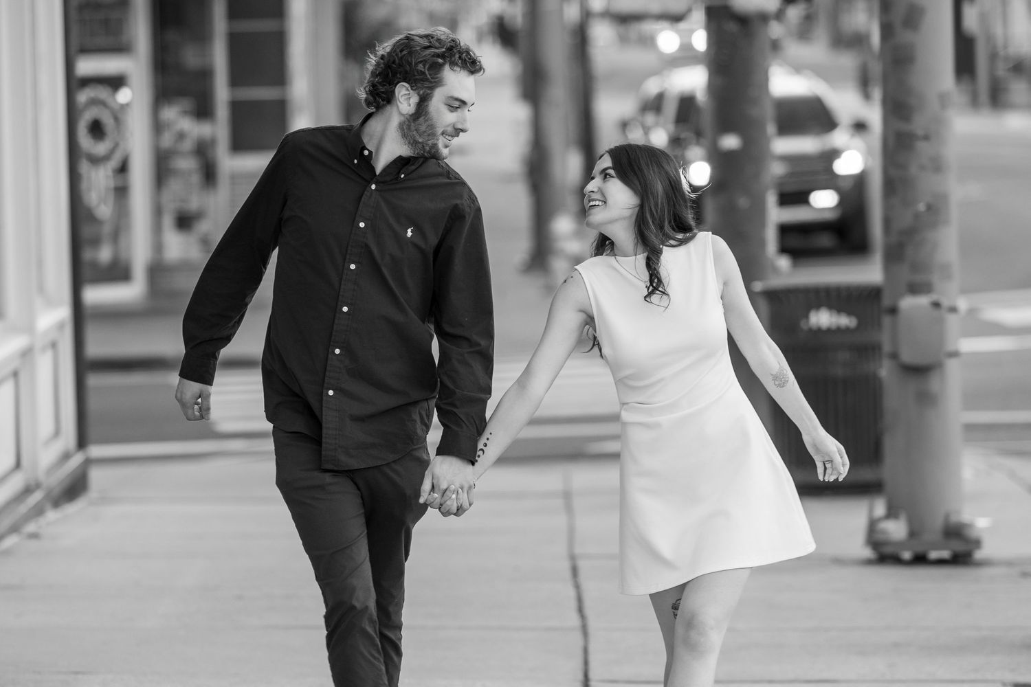 A couple in wedding attire walks hand in hand down a city street in black and white photography.