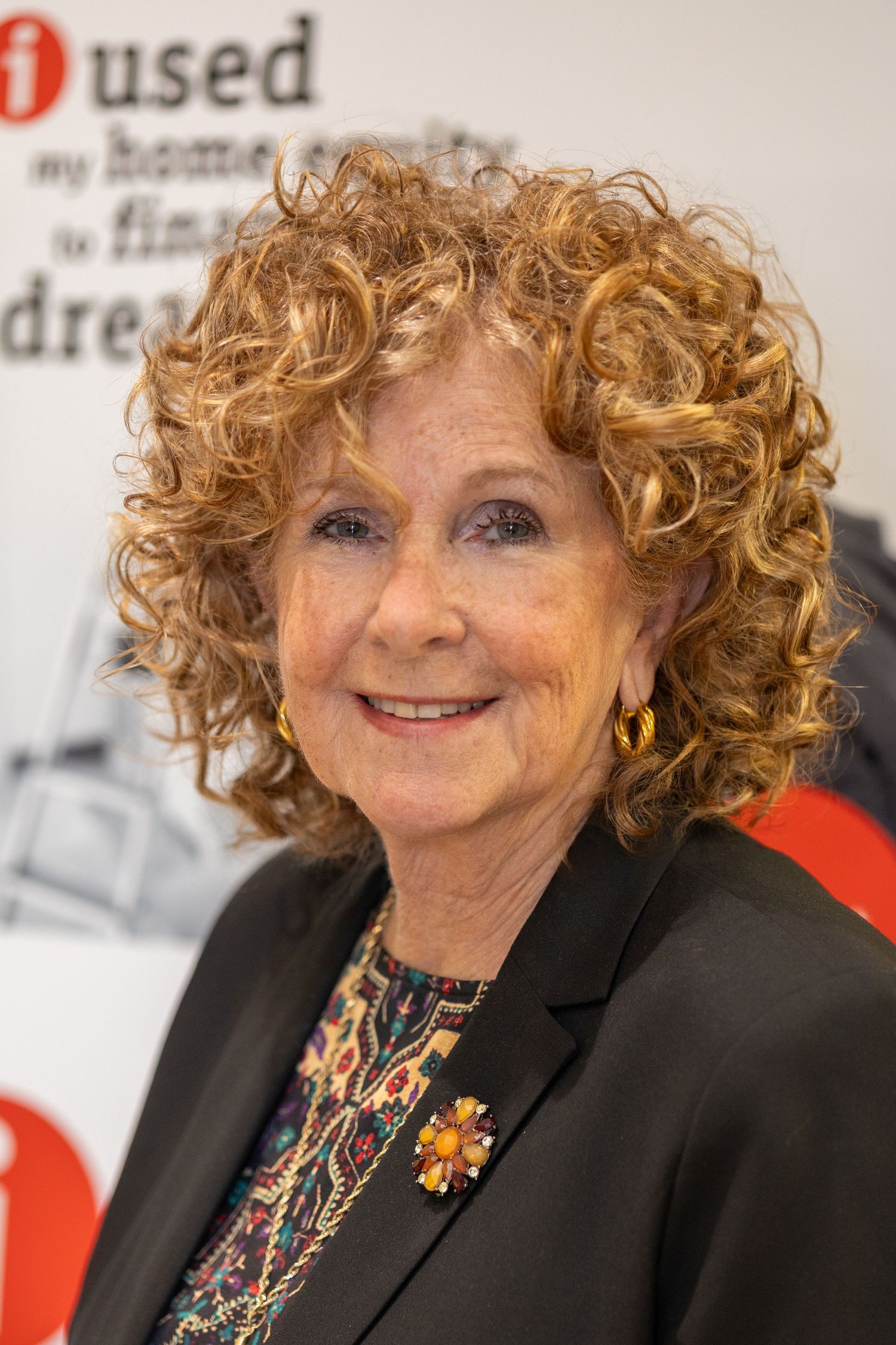 Portrait of woman with curly ginger hair wearing black blazer and colorful necklace.