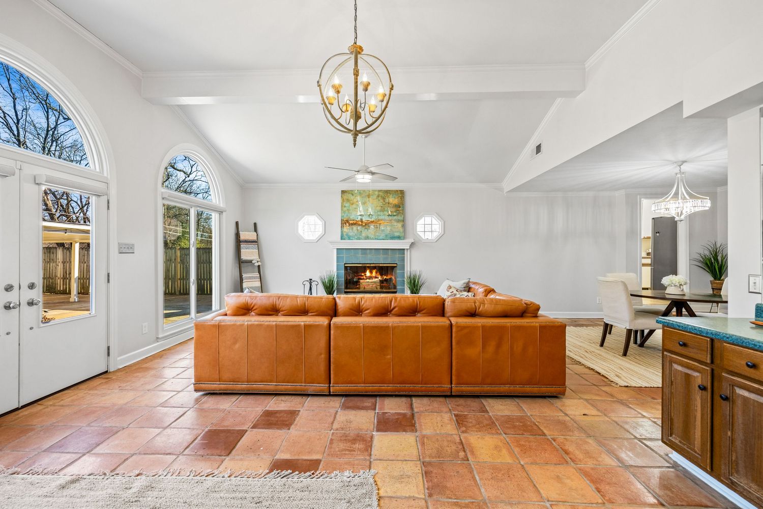 Open concept living space with orange sofa, hardwood floors, and modern chandelier in bright white interior.