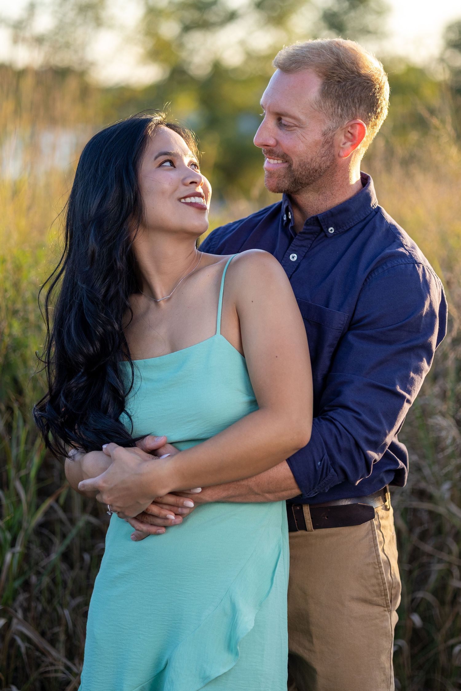 A couple laughs together during a sunset photoshoot in a field.