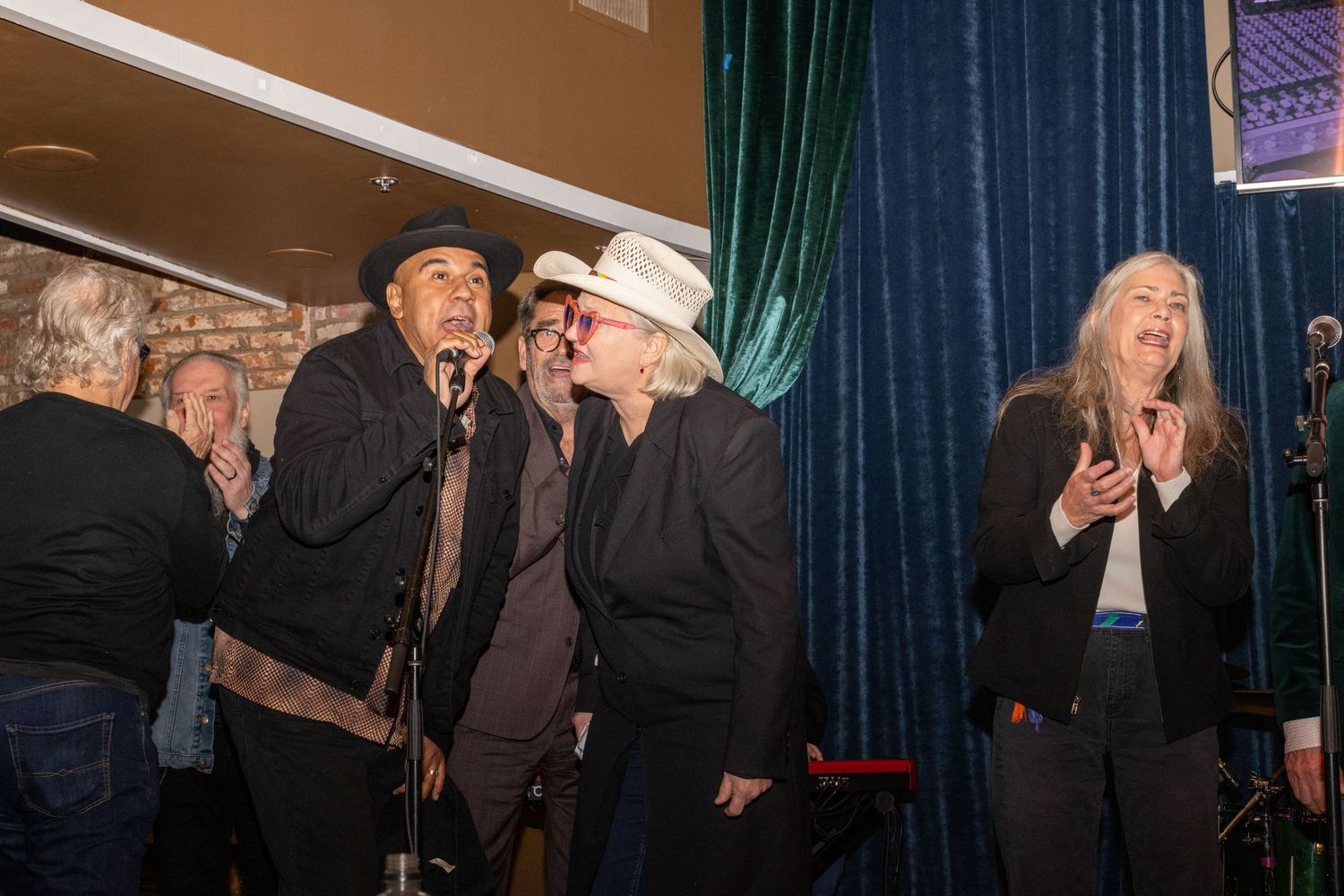 Live musical performance with multiple performers on stage against dark curtains.