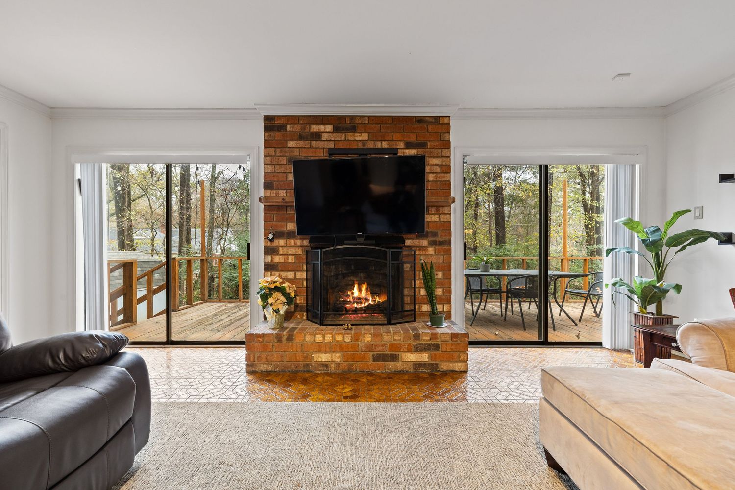 Spacious living area with brick fireplace, large windows overlooking wooded area, and hardwood floors.