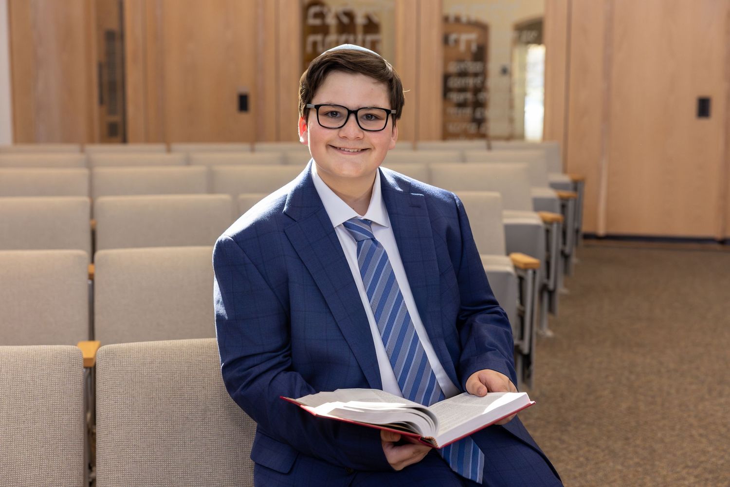 Professional in a navy suit and glasses sits at a desk while reading through business documents.