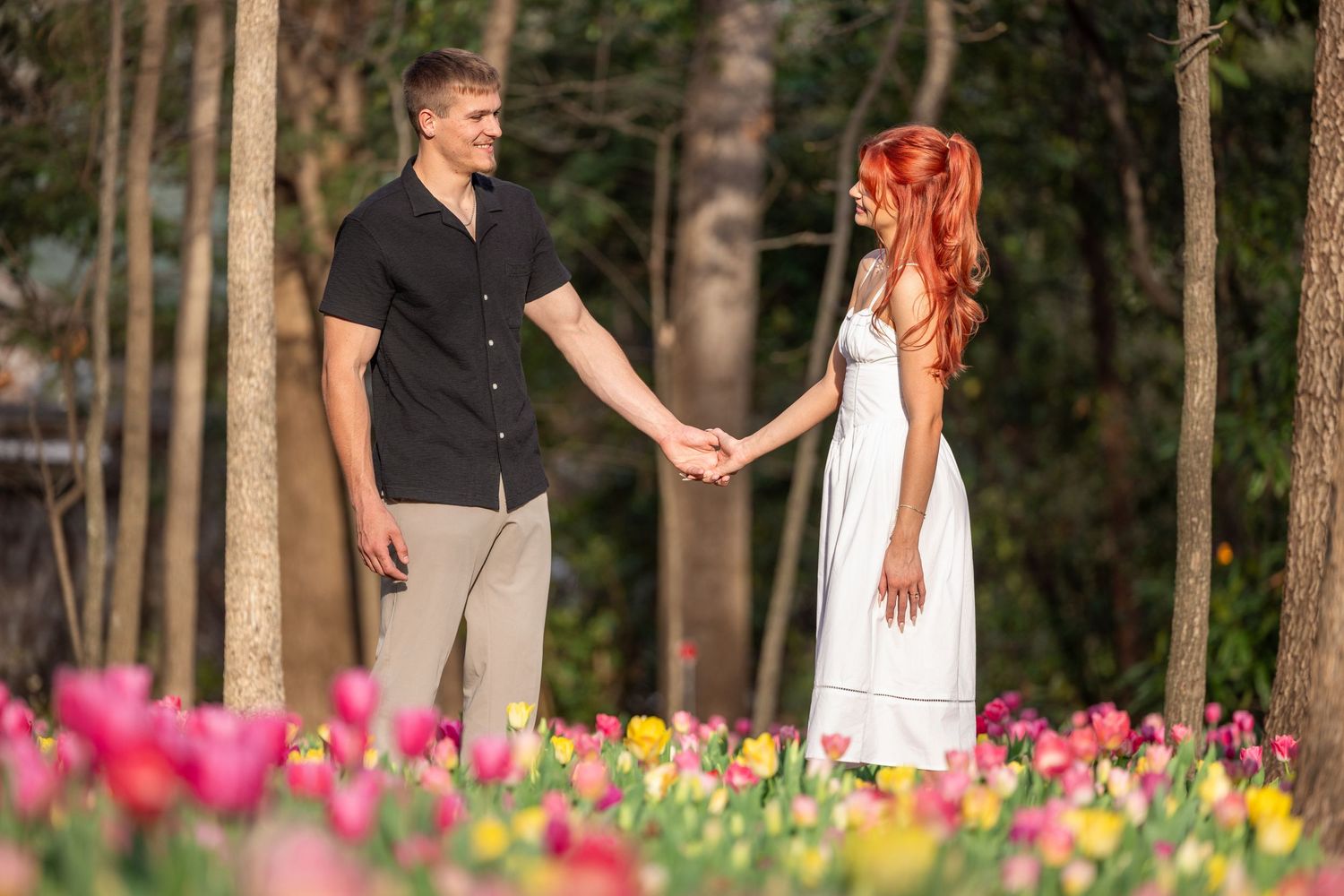 Couple holding hands while standing in a spring garden with blooming tulips and trees.