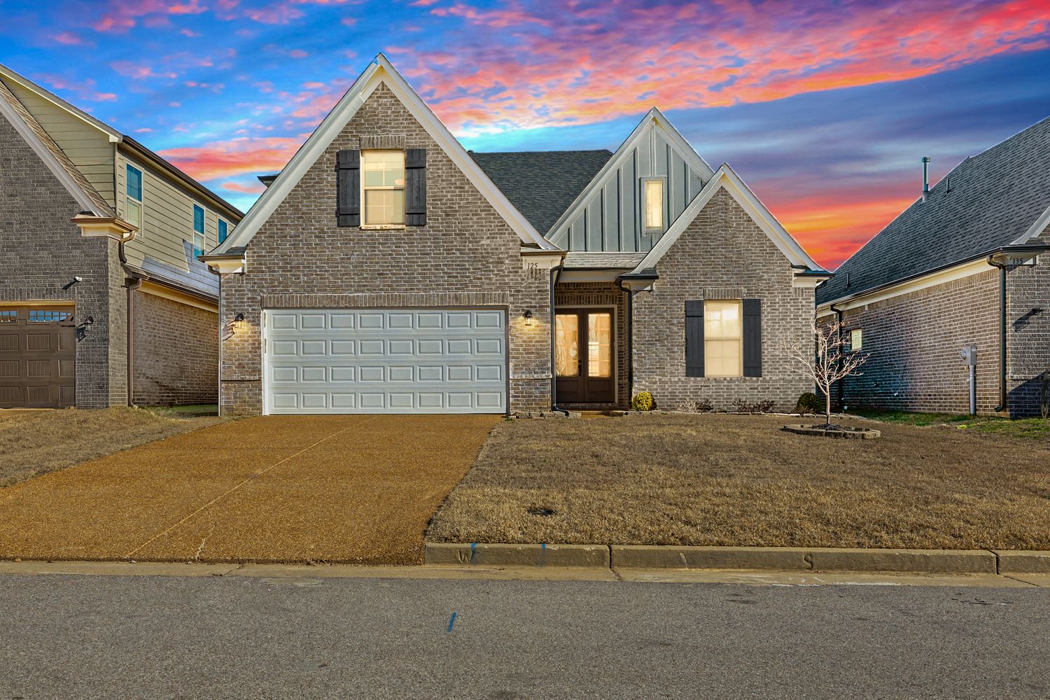 Modern gray suburban house with peaked roof and garage illuminated at sunset with dramatic pink and purple sky.