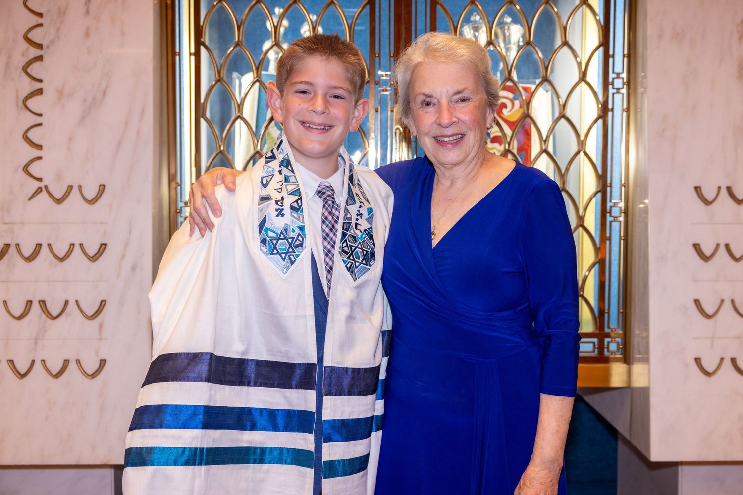Two people in formal attire pose together at an elegant event with decorative wall panels in the background.