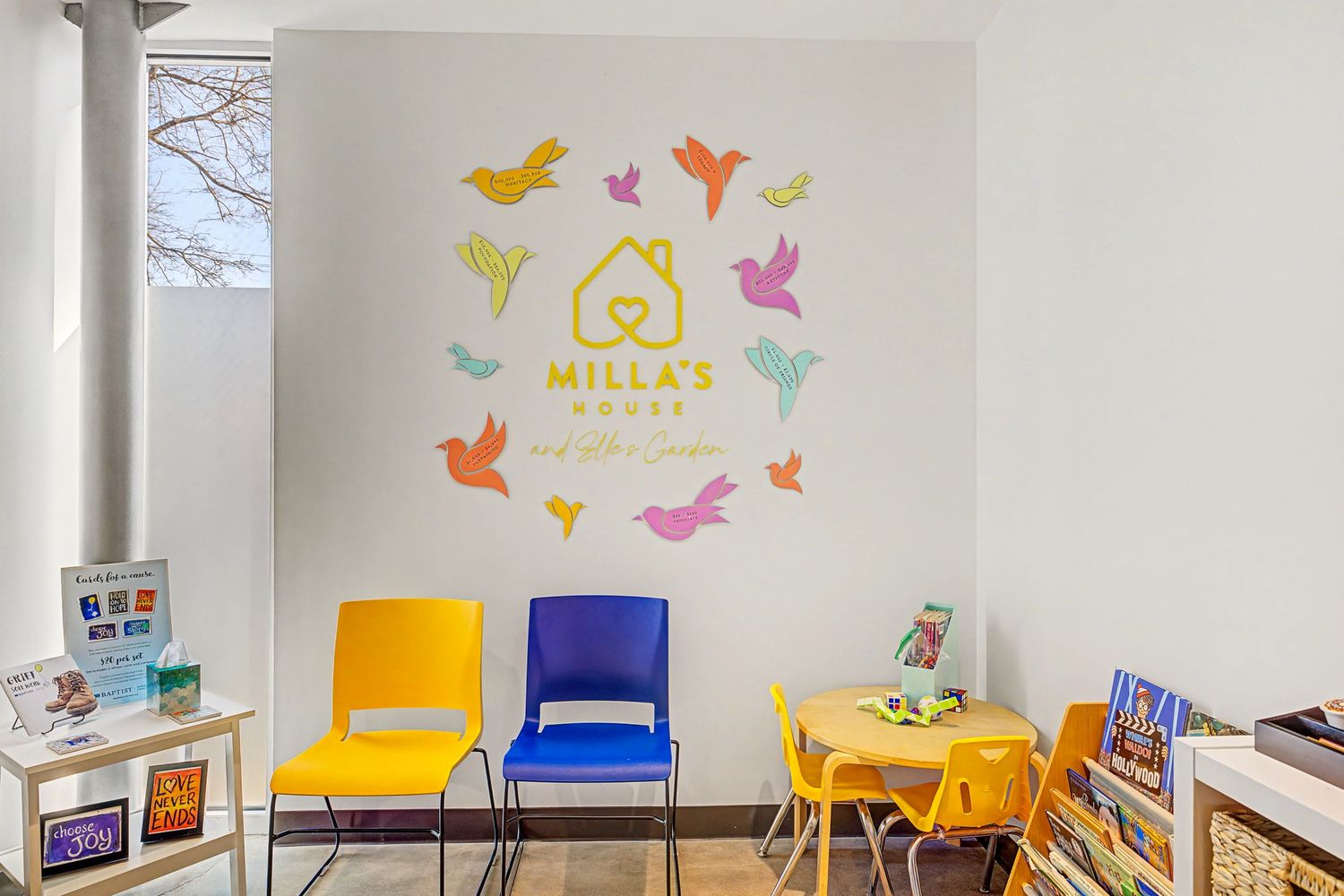 Colorful waiting area at Milla's House with yellow, blue chairs, kids table, and bird wall decal logo.