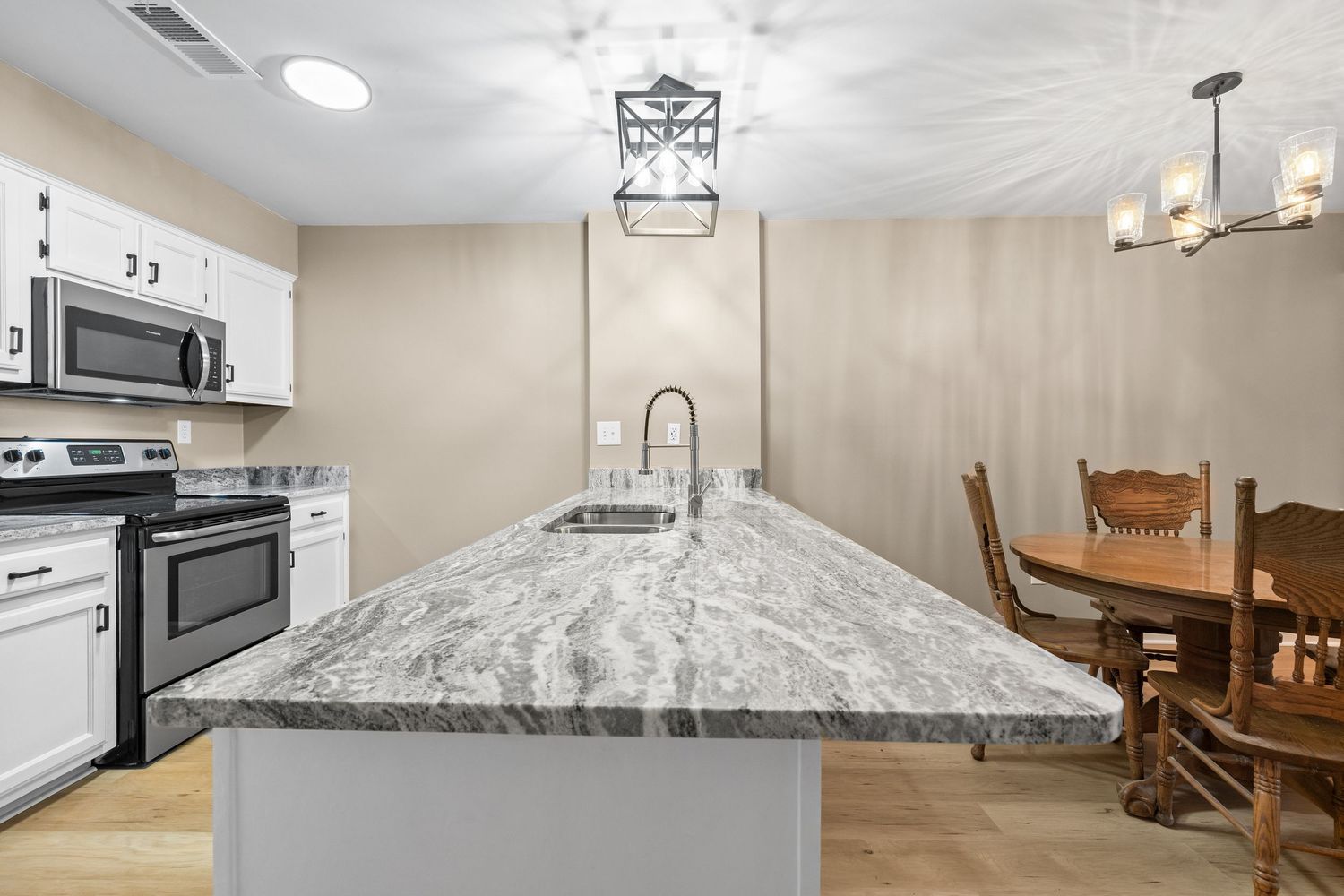 Spacious kitchen with gray marble countertops and modern black pendant lighting fixtures.
