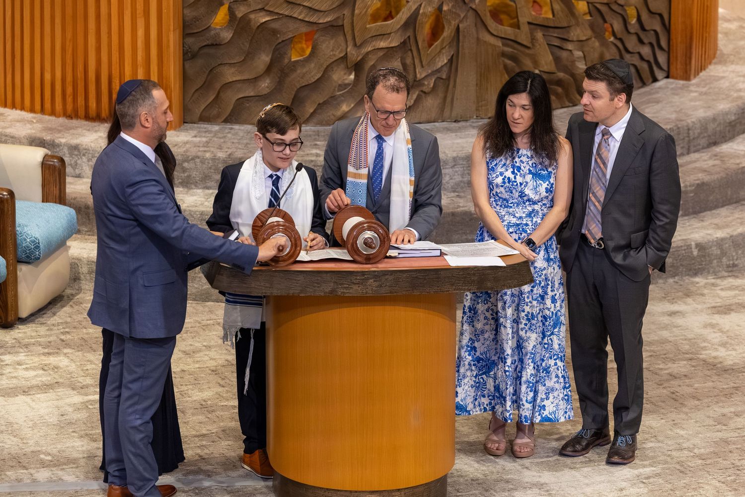 Family gathered around a Torah scroll during a Bar Mitzvah ceremony at a synagogue.