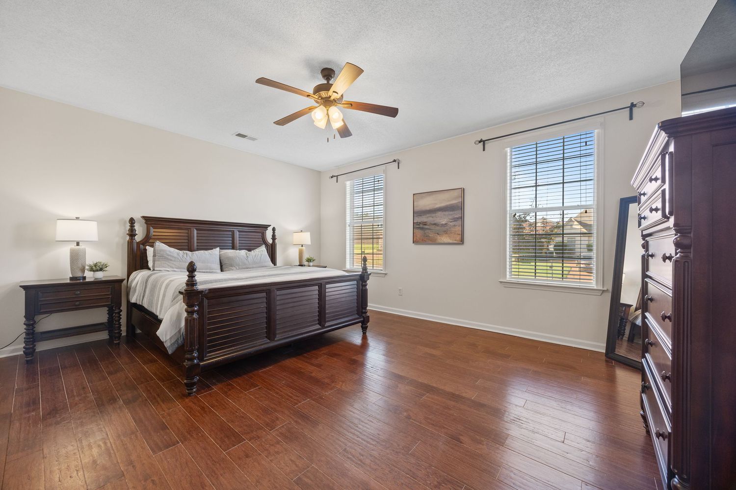 Interior photo showing hardwood floors and ceiling fan in an empty residential room with white walls and natural lighting.